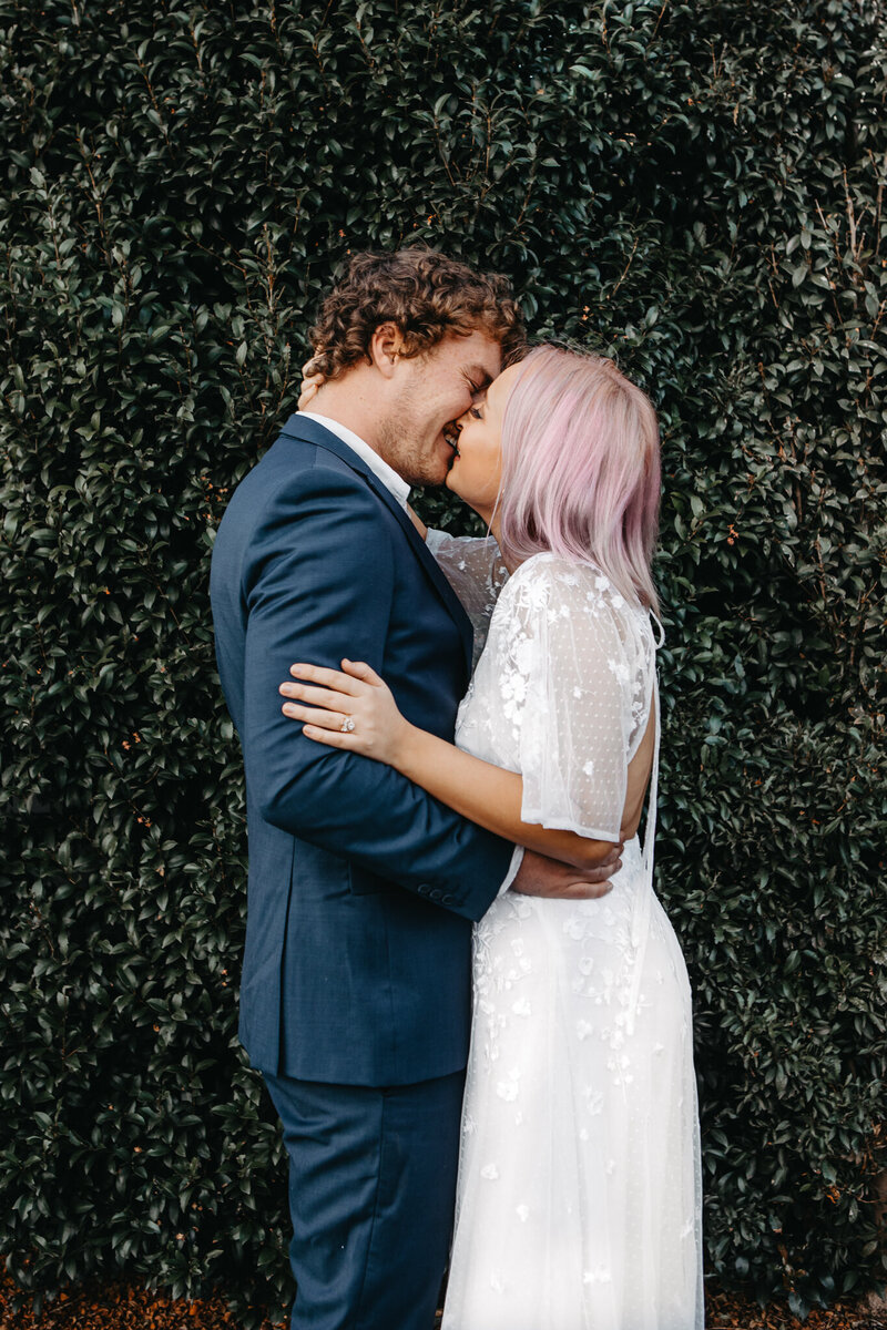 modern bride and groom share a kiss in front of grass wall