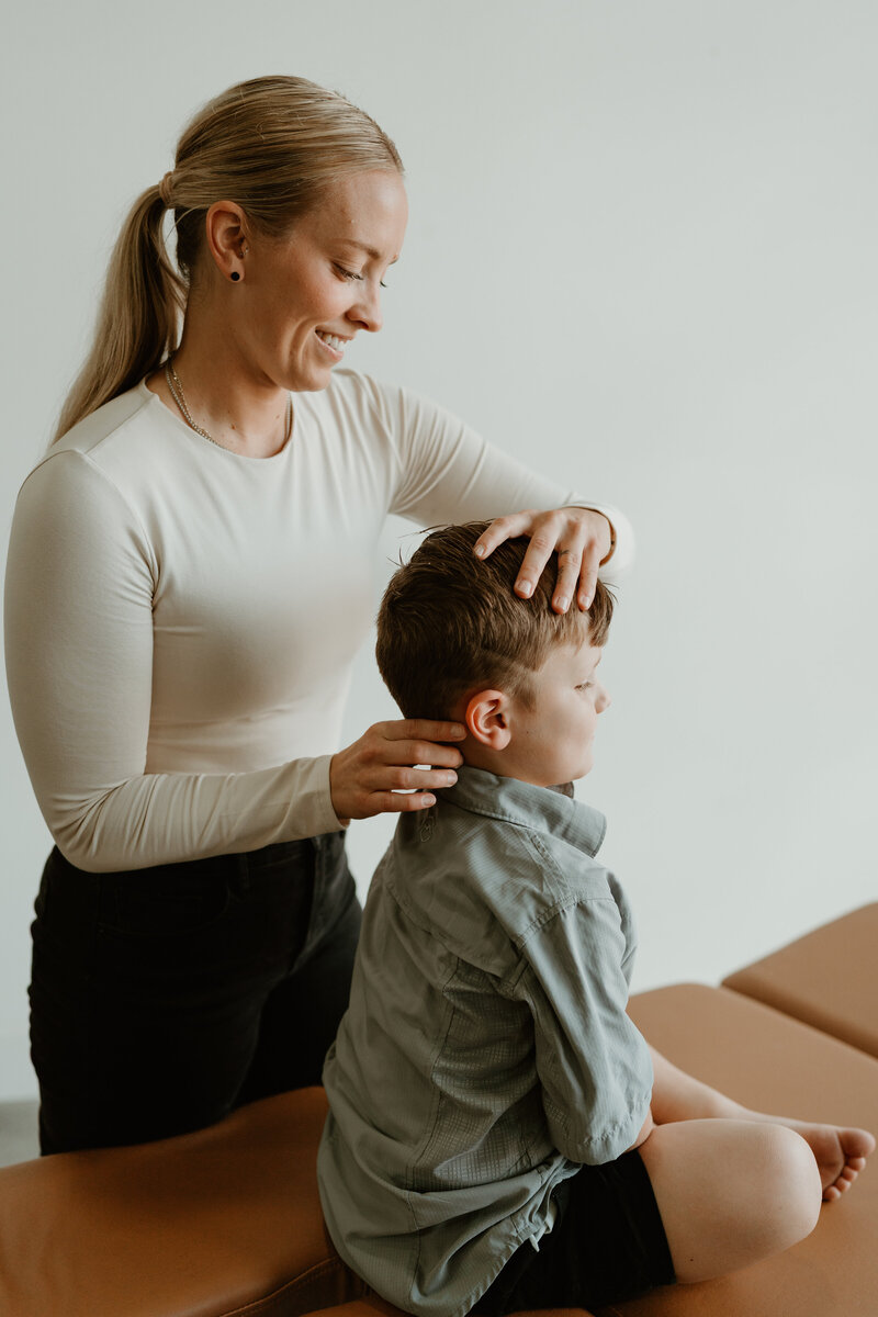 woman adjusting young boy on chiropractic table