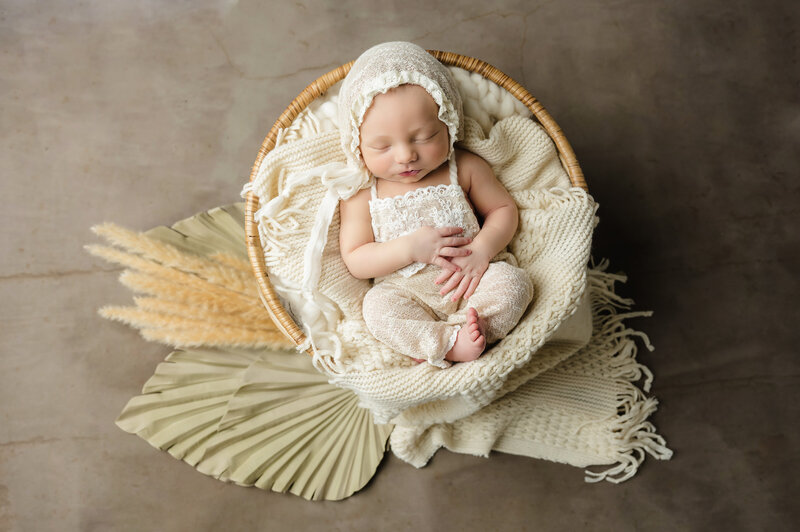 baby girl wrapped in blue with floral crown sleeps on mini papasan chair surrounded by flowers
