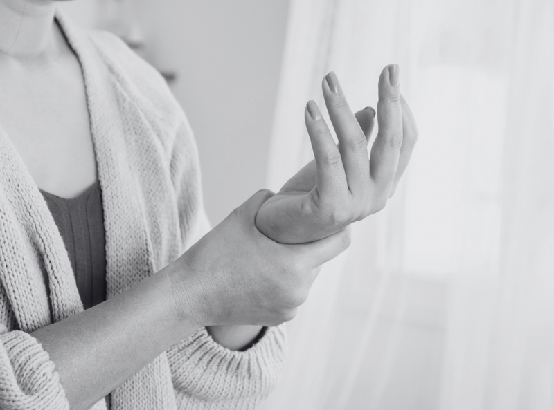 Woman holding her wrist, possibly experiencing pain or discomfort, in a close-up black-and-white image.
