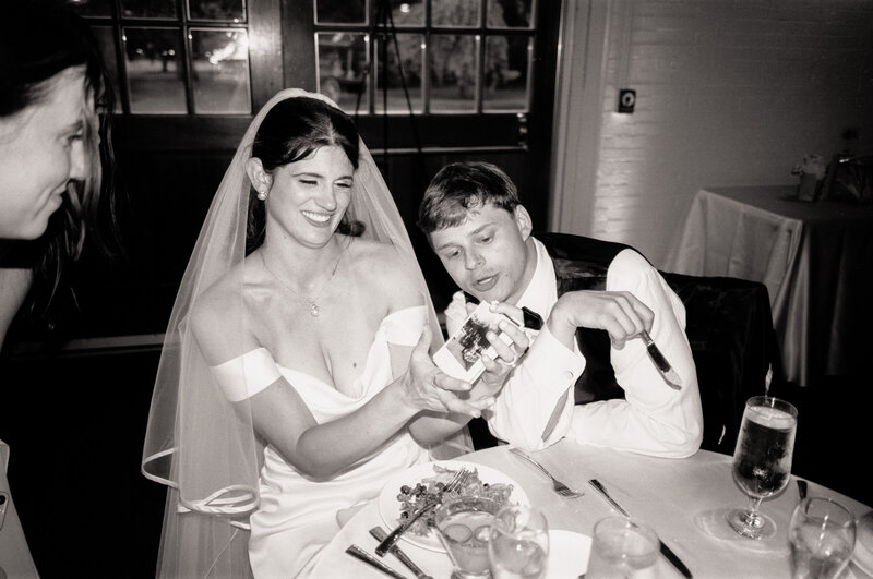 Black and white film photo of a bride and groom laughing as they look through Polaroids at their reception during a wedding at the Garden at Elm Bank in Massachusetts — a candid analog moment made by a film wedding photographer.