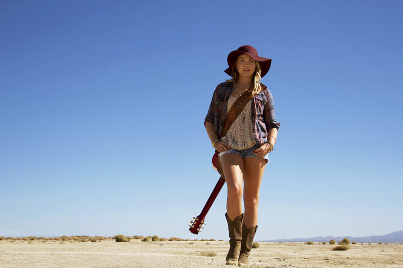 Musician portrait Danielle Marie walking in desert guitar slung across her shoulder