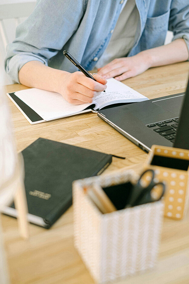 A woman writing in a notebook at a desk, focused on her website to-do list.
