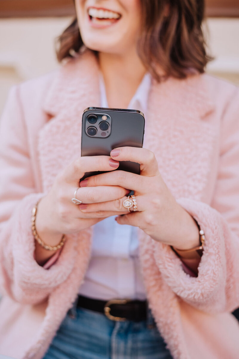 A close-up of Madison’s hands holding a phone in a pink textured coat—representing connection, strategy, and personal support in digital partnerships.