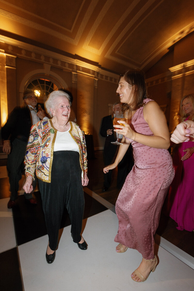 elderly woman dancing with woman in pink dress at wedding reception