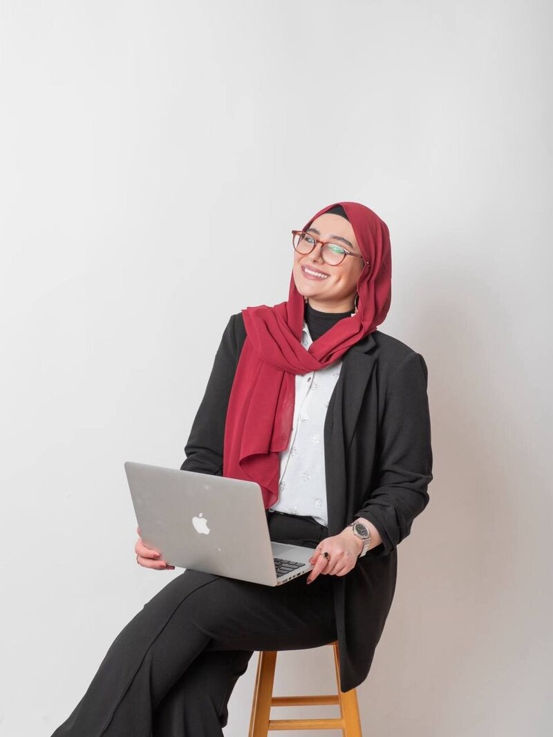 Ayah Official smiling while working on her laptop, mentoring women entrepreneurs to build online businesses with authority and confidence.