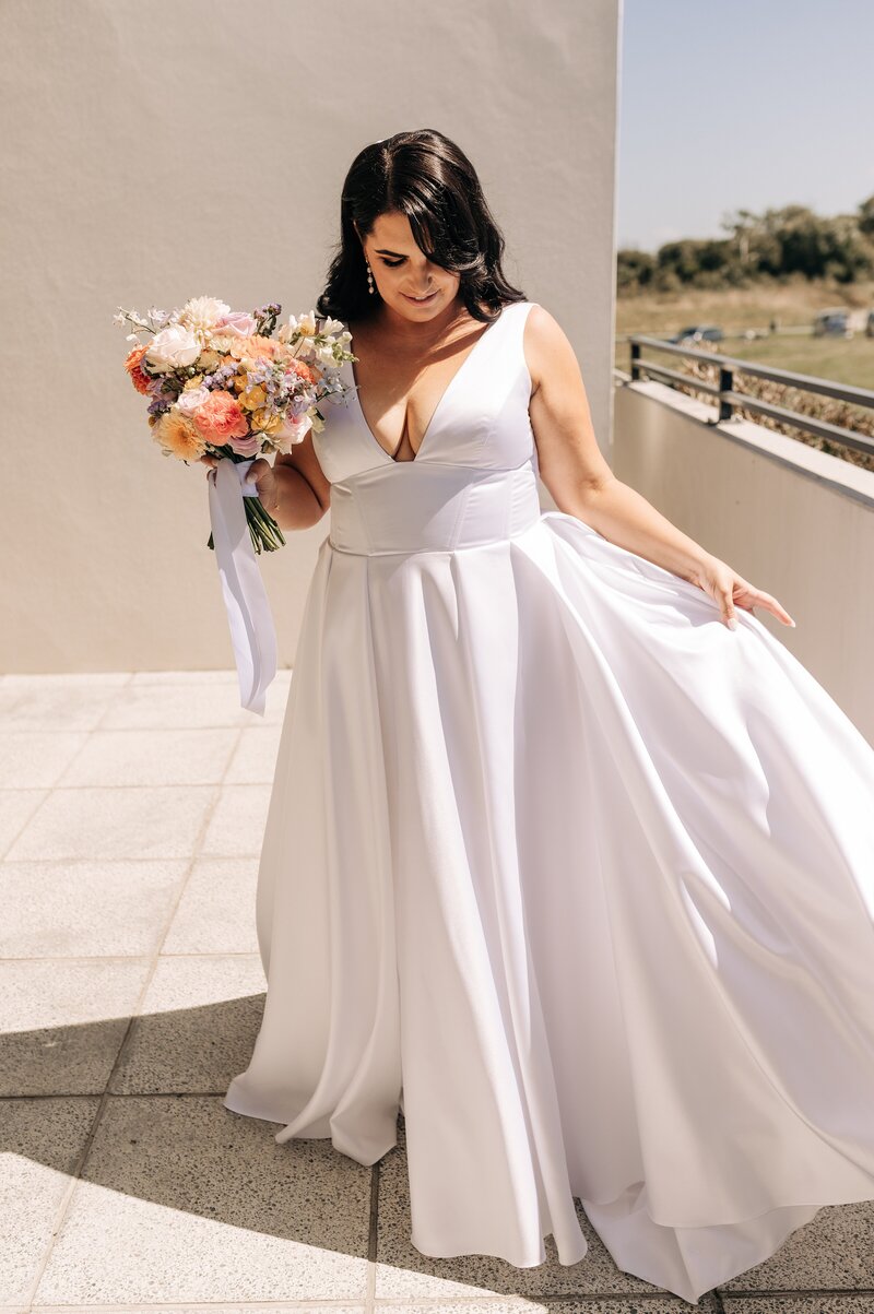 ellie fitzgerald wedding bride holding white gown and pastel bouquet on sunny balcony