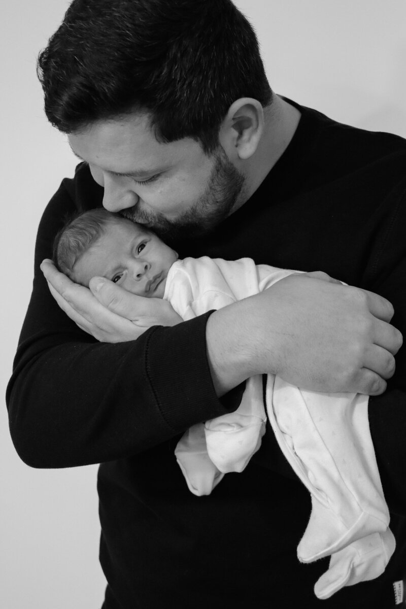 Black and white photo of father holding newborn baby in natural light home session Buxton 