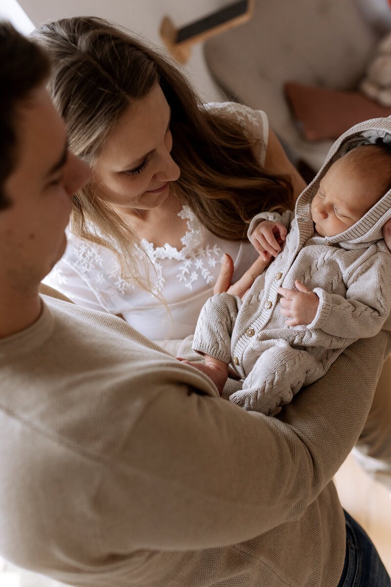 Eltern halten Baby auf dem Arm und gucken es an