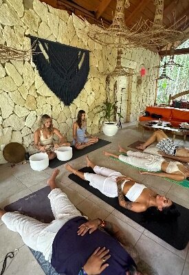 Sheldan Paige guiding a small group yoga and sound healing session in a shaded outdoor space in the jungle near Tulum, using crystal bowls and intentional movement.