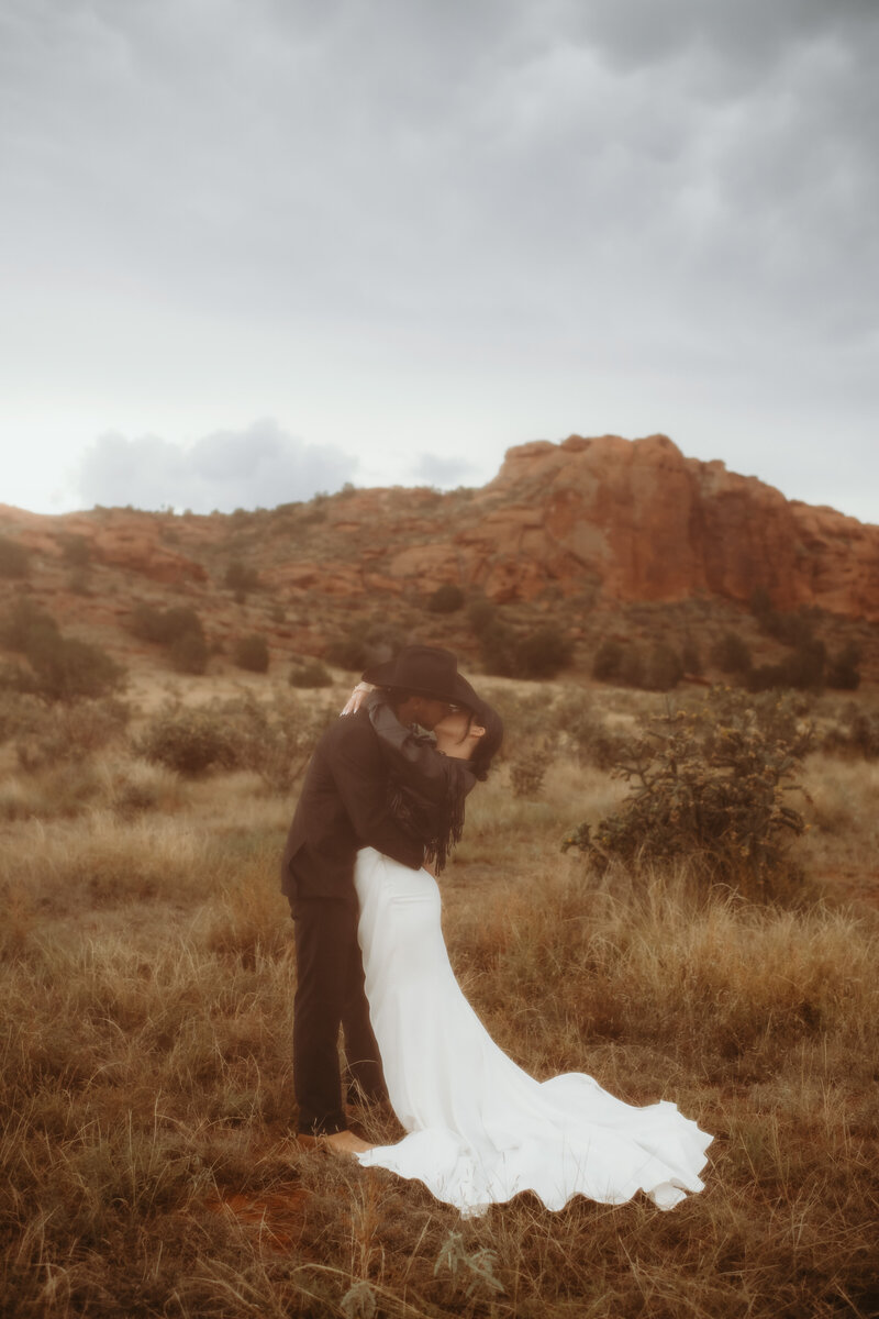 couple dip kissing with the red rocks in the background at their ranch wedding