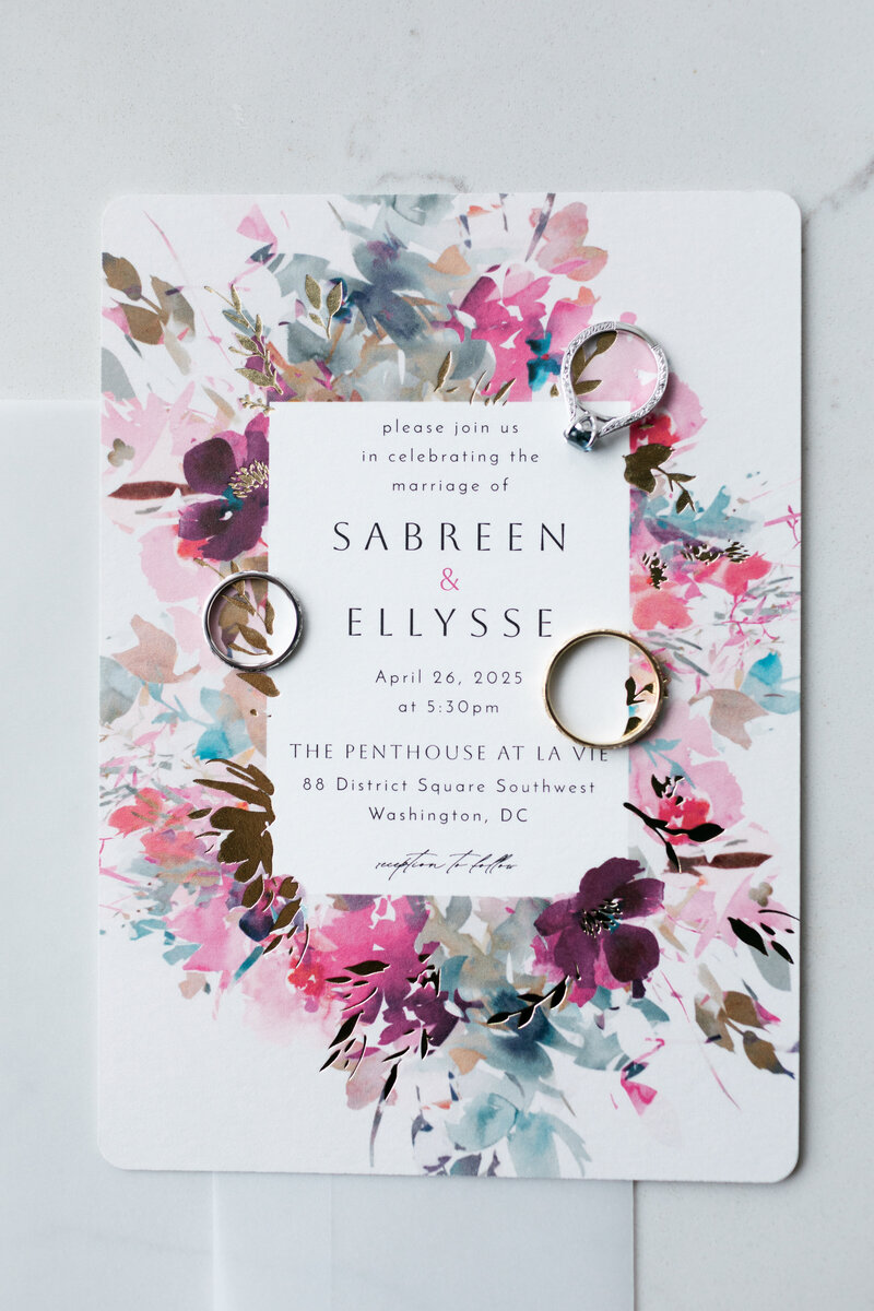 flat lay of RSVP invitation for Sabreen and Ellysse with their wedding rings on top of the invite