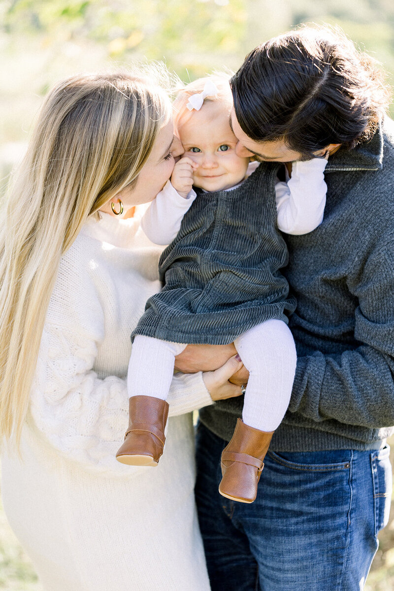 Image of two parents kissing their baby on each cheek while holding her between their torsos
