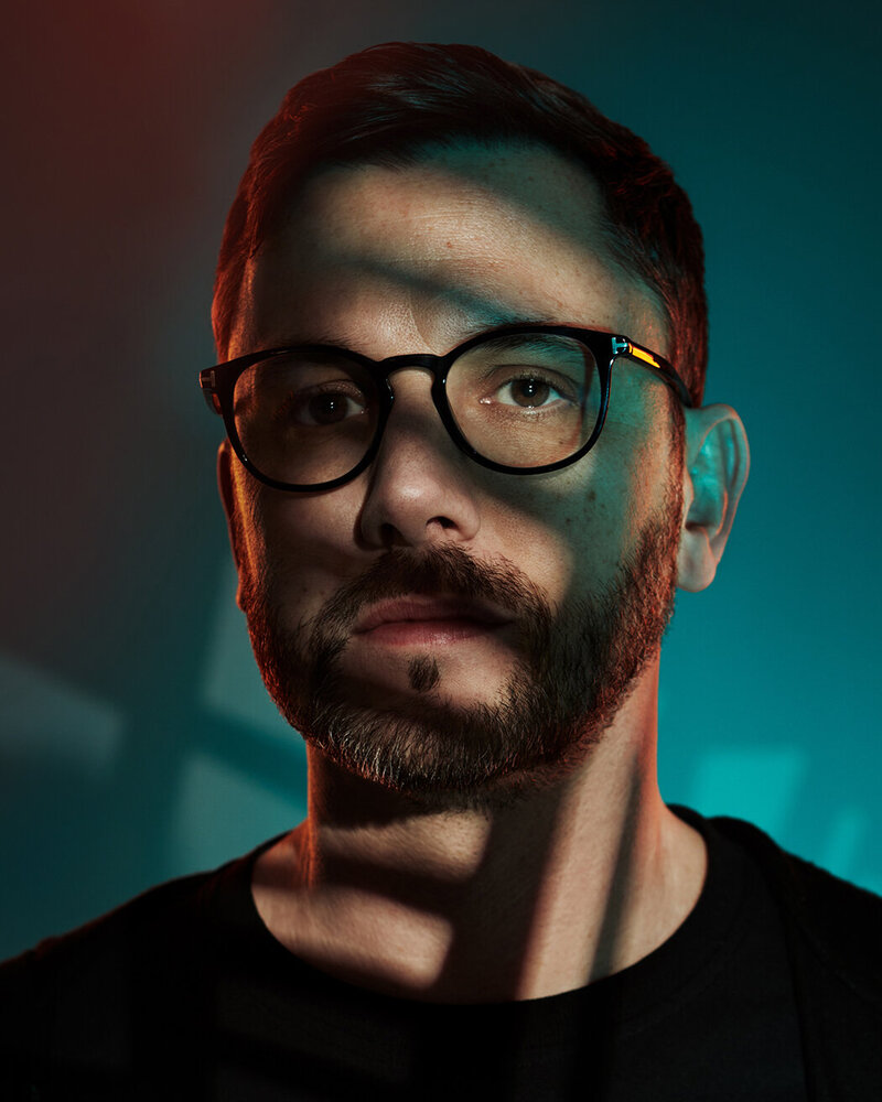 Moody studio portrait of Mike Ball with glasses, featuring dramatic shadow and light effects, captured by Ylva Erevall.