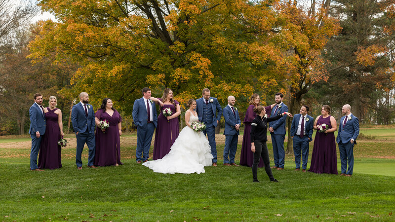 Photographer coordinating a large bridal party for a posed photo on a scenic golf course in the vibrant colors of autumn.