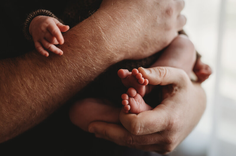 dad's hands holding his newborns tiny little feet.