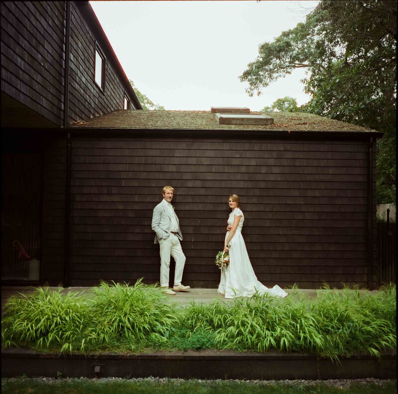 A bride and groom smile together for a photo in front of a stylish black house.