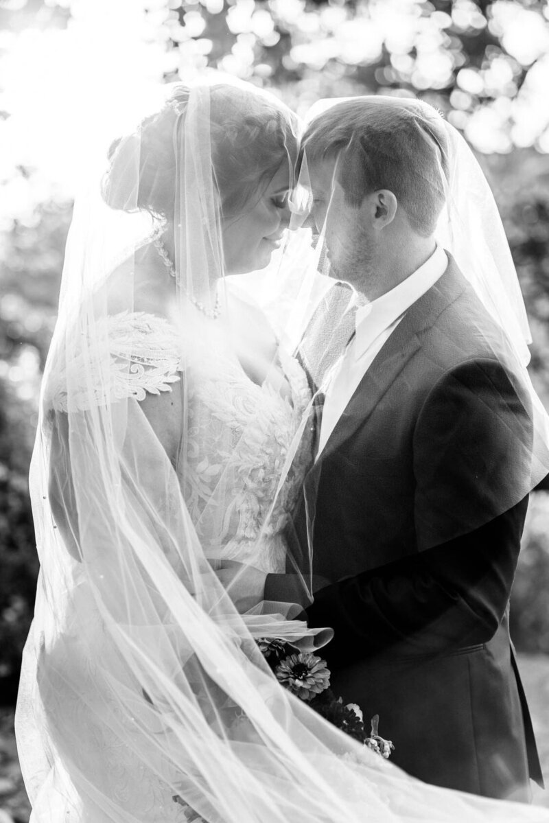 bride and spouse posed under her custom pearl bridal veil and blusher in black and white