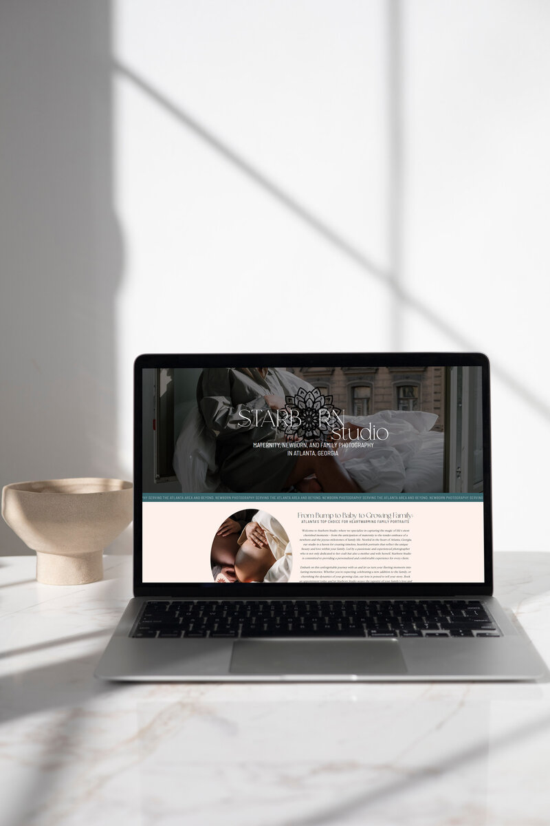 A laptop on a countertop in a sunny room with the screen showing the hero section of the about section of the starborn studio website in a mock up
