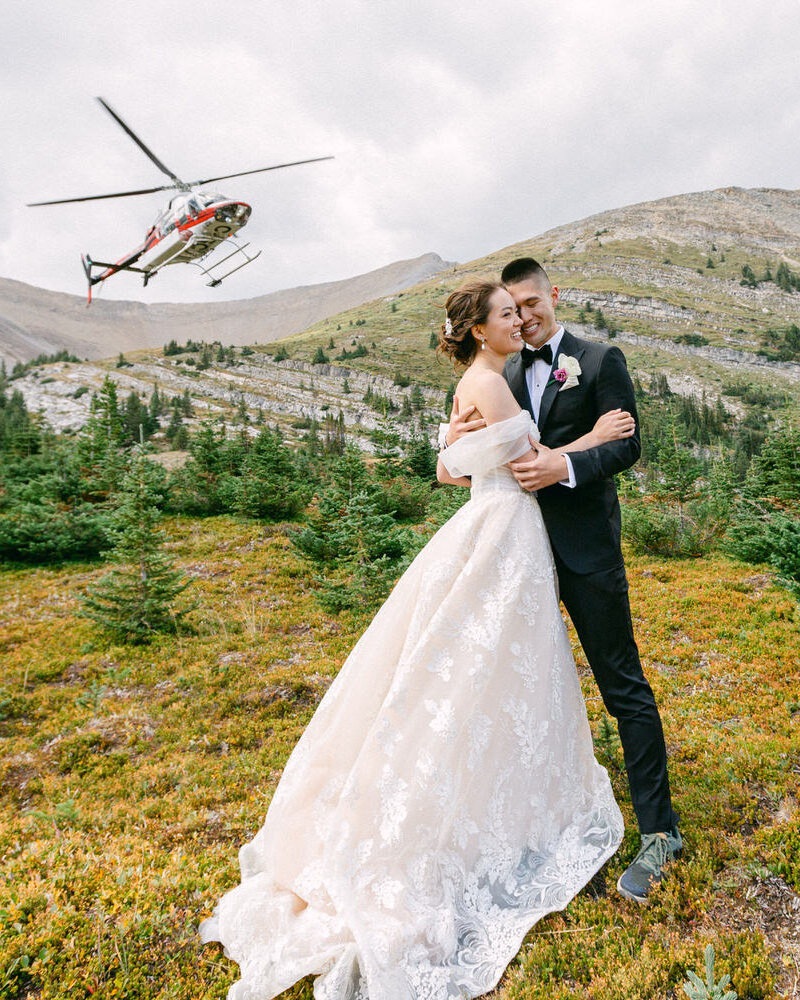 This breathtaking photograph captures the bride and groom kissing with joy after their luxury elopement in Banff National Park. Having just landed from their private helicopter, the stunning mountain landscape surrounds them, creating an unforgettable moment of celebration and love.