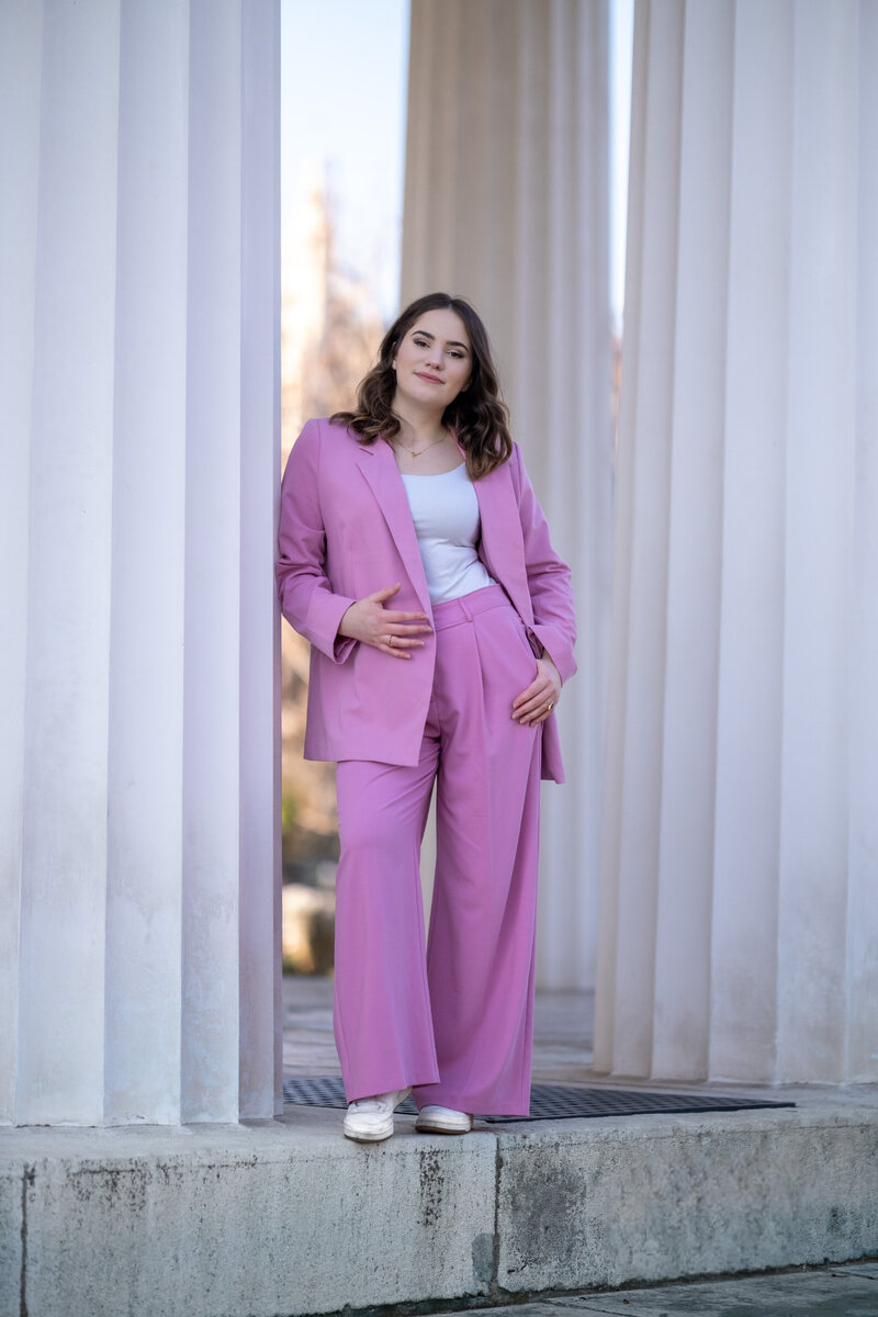 Founder in pink suit leaning on the white column, smiling