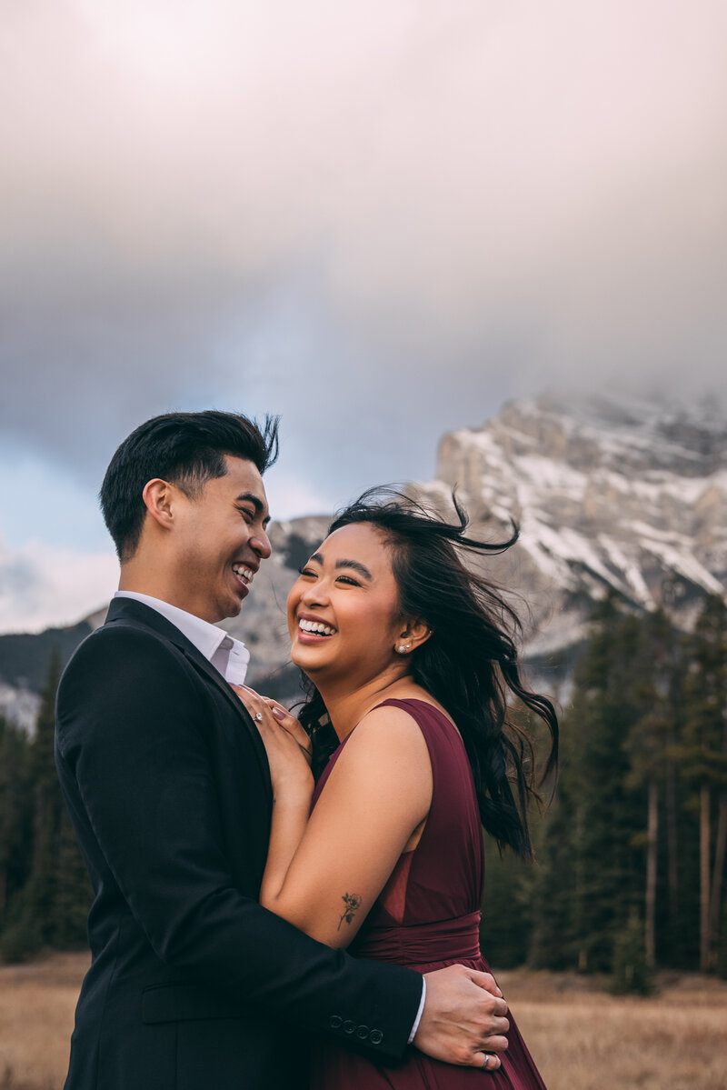 A couple in each others arms laughing with a mountain in the background