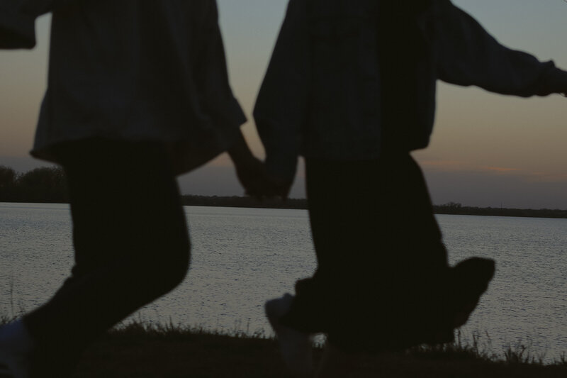 A couple are running while holding hands. It is just their lower bodies that are showing. Their bodies are shadowed as the sunset can be seen in the background