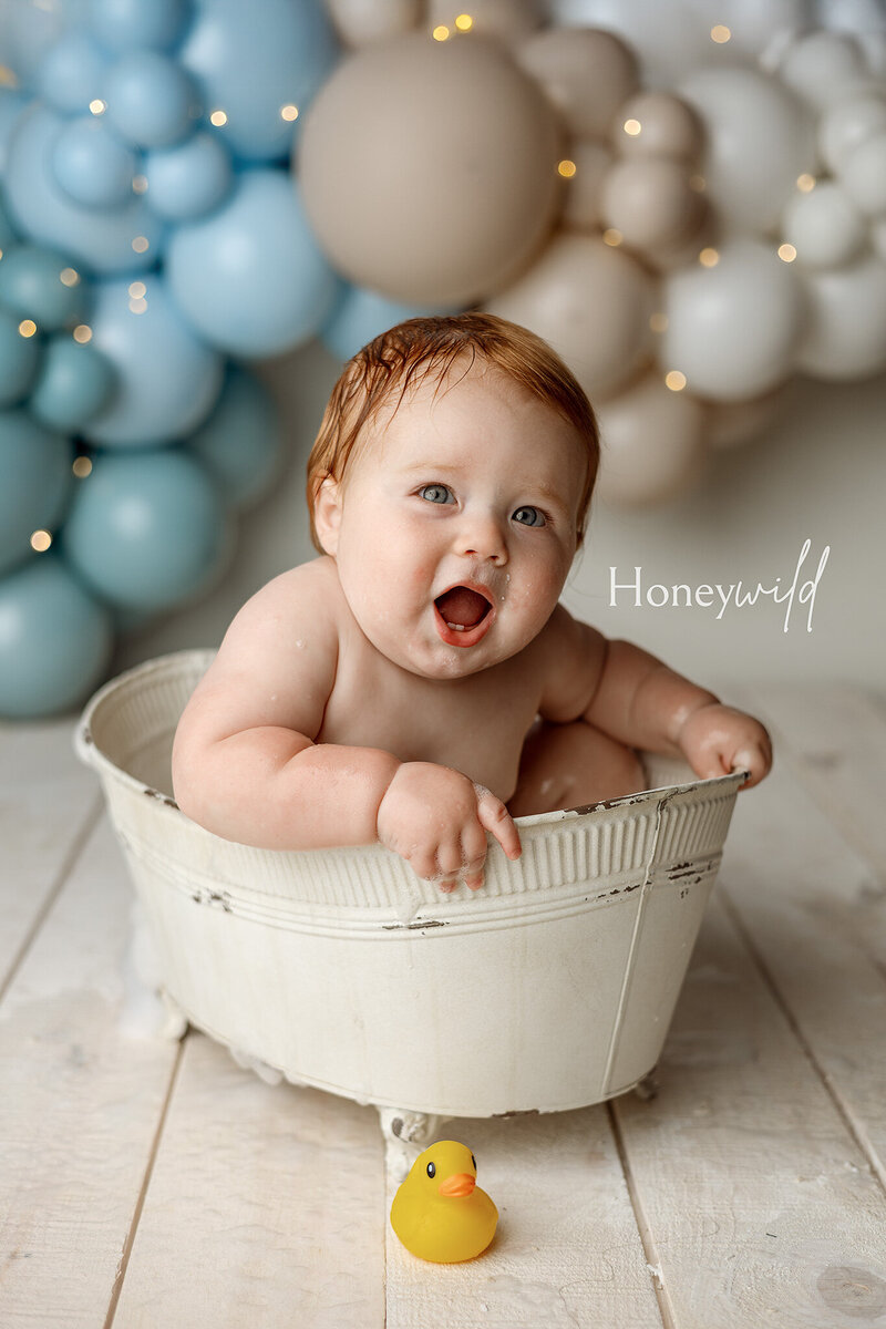 Newborn baby swaddled in a white knit wrap, peacefully sleeping in a wicker basket on a rustic wood floor. Photographed by Honeywild Photography, a luxury newborn photographer in Grand Rapids, MI, specializing in timeless and elegant portraits