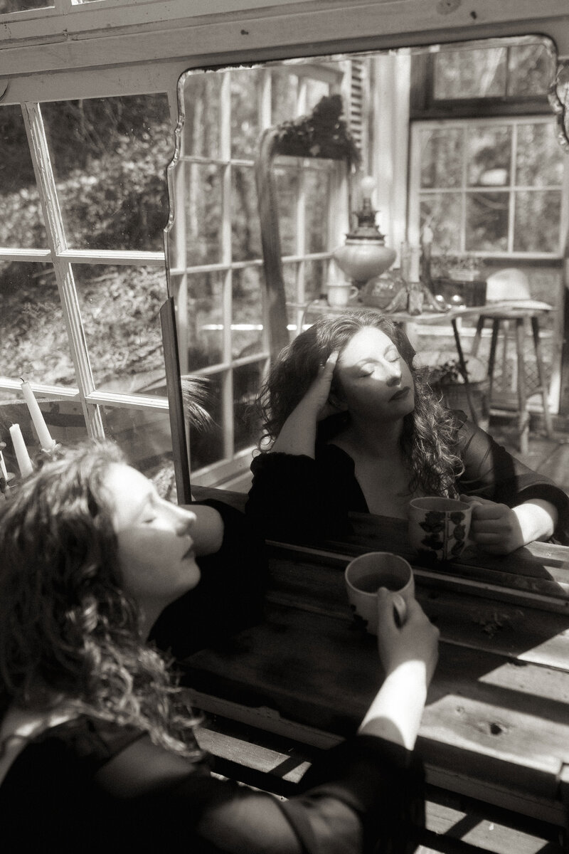 A woman sitting in a glass shack in front of a mirror closing her eyes to take in the moment. 