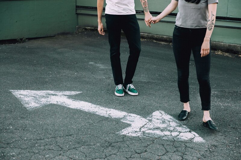 2 teens holding hands in black pants with arrow on street