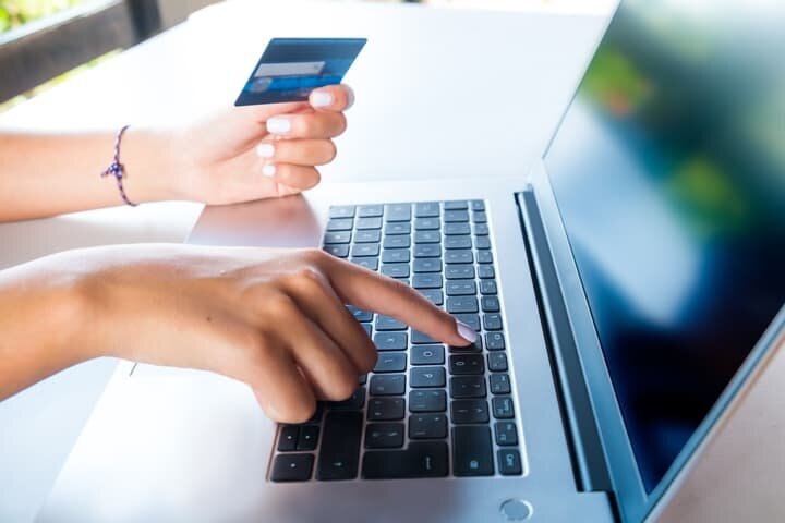 Author making online payment for book publishing services, holding credit card while using laptop