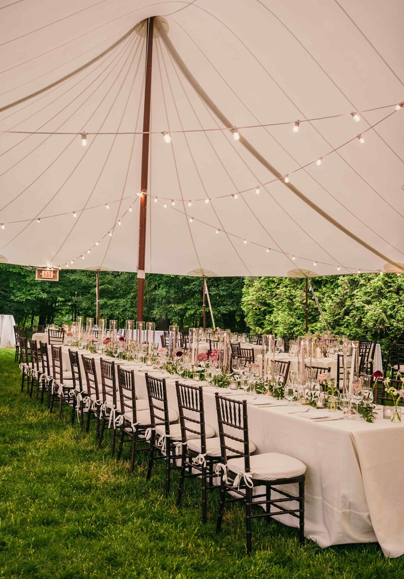 A charming outdoor tented wedding in Franklin Lakes, NJ, with a long banquet table set under a canopy of twinkling string lights.