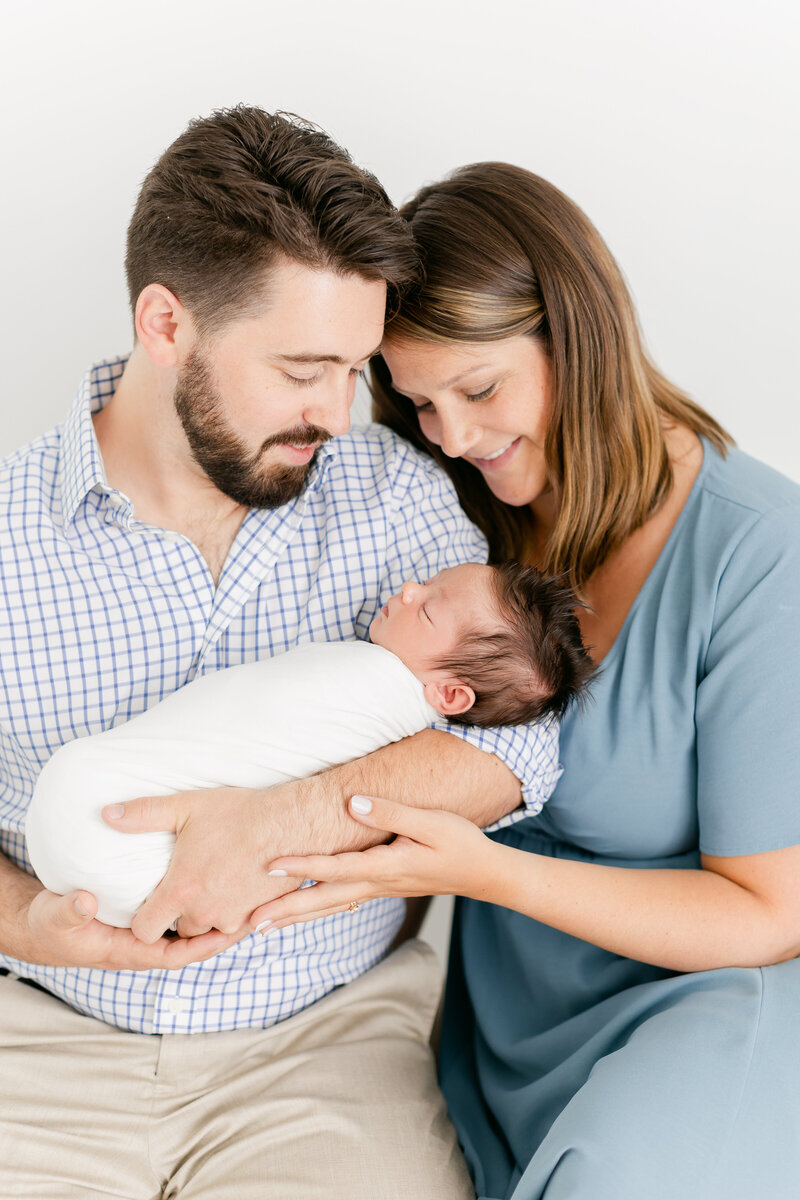 A mother and father holding their newborn baby on a bench while smiling down at him by Washington DC Photographer