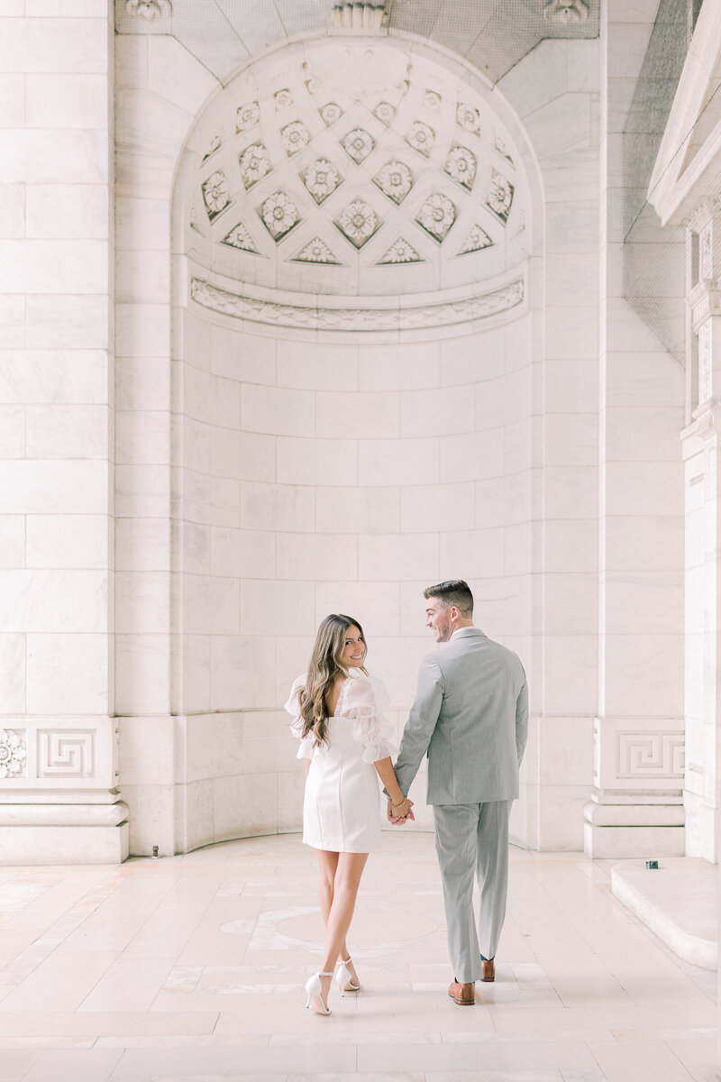 Couple holding hands and walking in front of a white wall with high ceilings