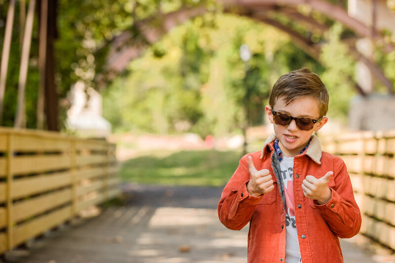 A little boy wearing an orange shirt giving a cheerful thumbs up during a vibrant photography mini session in Phoenixville