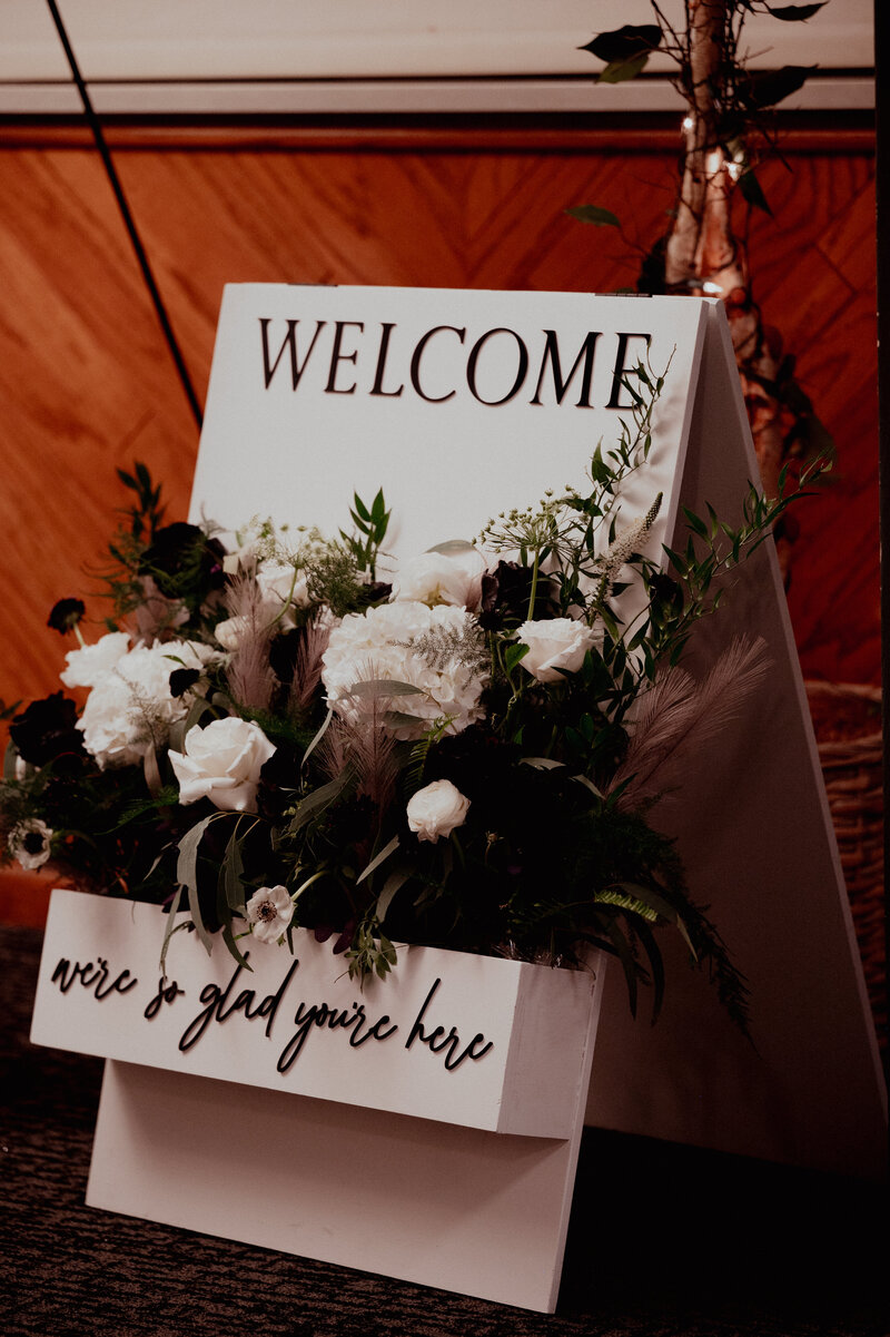 A-frame wedding welcome sign with floral box filled with large white flowers and full greenery