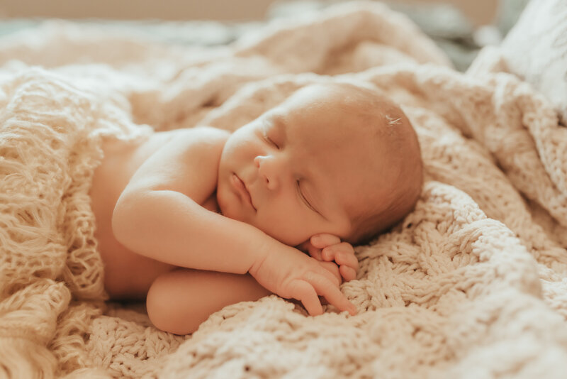 A sleeping newborn baby wrapped in a white crocheted blanket.