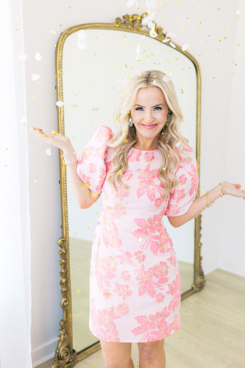 Woman smiles in pink and white  floral dress with gold mirror in background