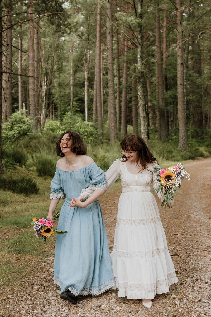 An LGBTQ+ hold hands together and walk through the Aberdeenshire woodlands. They launch candidly as they are photographed in wedding attire.