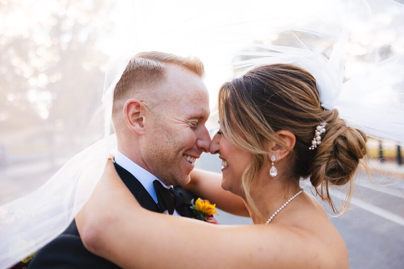 bride and groom holding one another smiling and laughing while touching noses underneath the brides veil in front of the united states capitol building 