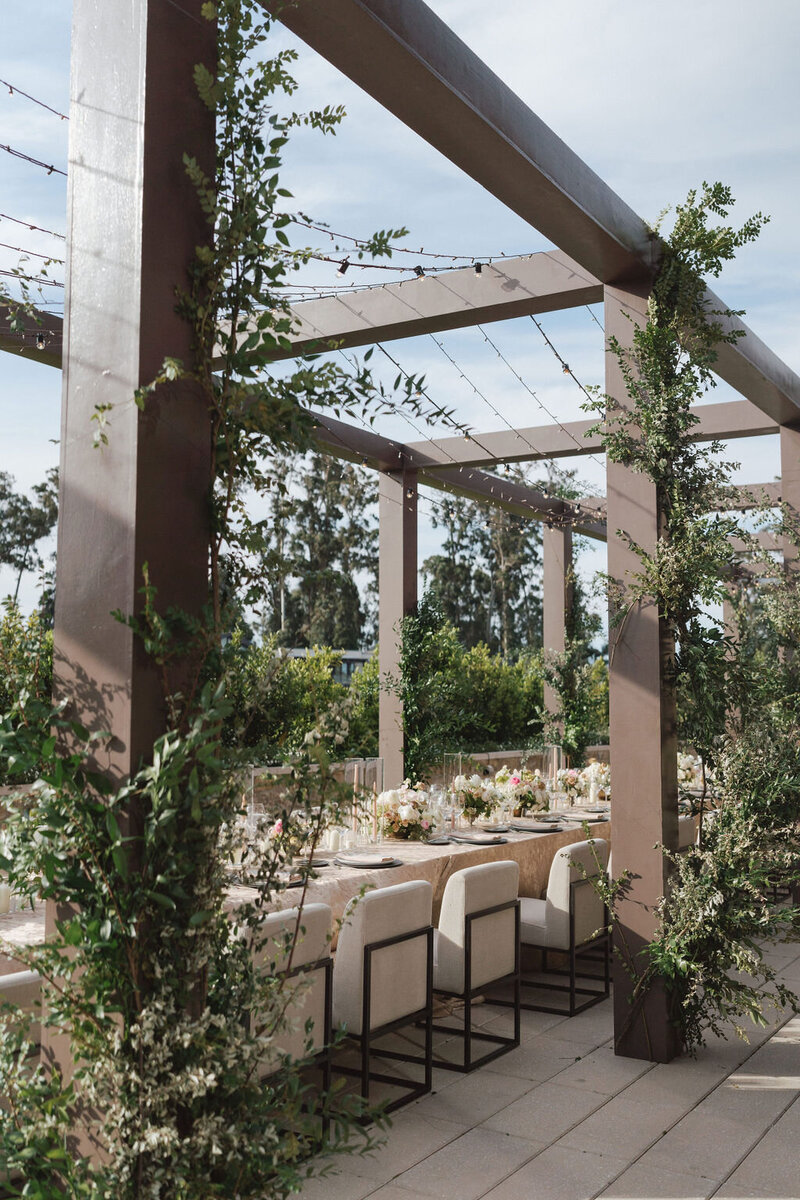 An elegant outdoor wedding reception space with a brown structure and greenery
