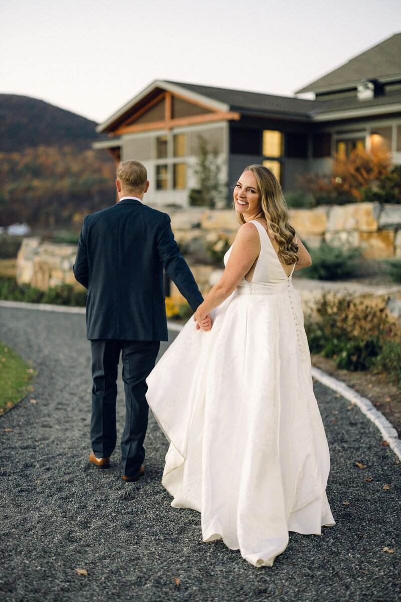 A bride looks back and smiles for the wedding photographer as the bride and groom walk to their wedding reception at the Ticonderoga Golf Course in the Adirondacks.