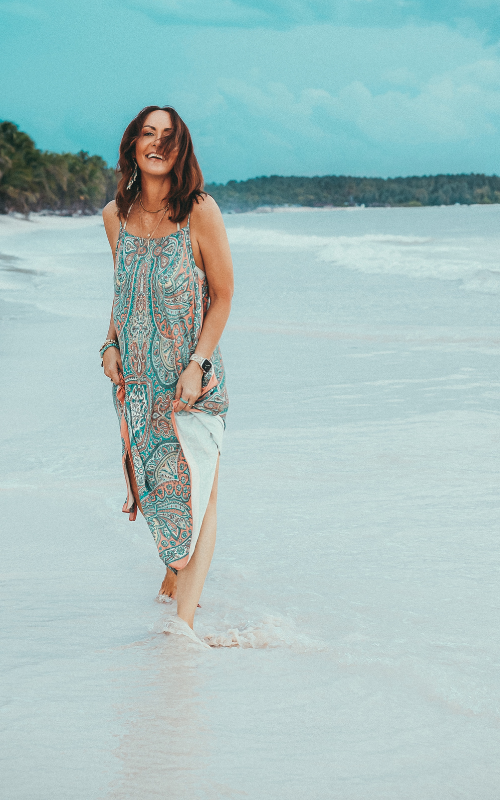 brunette woman smiling feeling free on the beach wearing a paisley dress mystical coach
