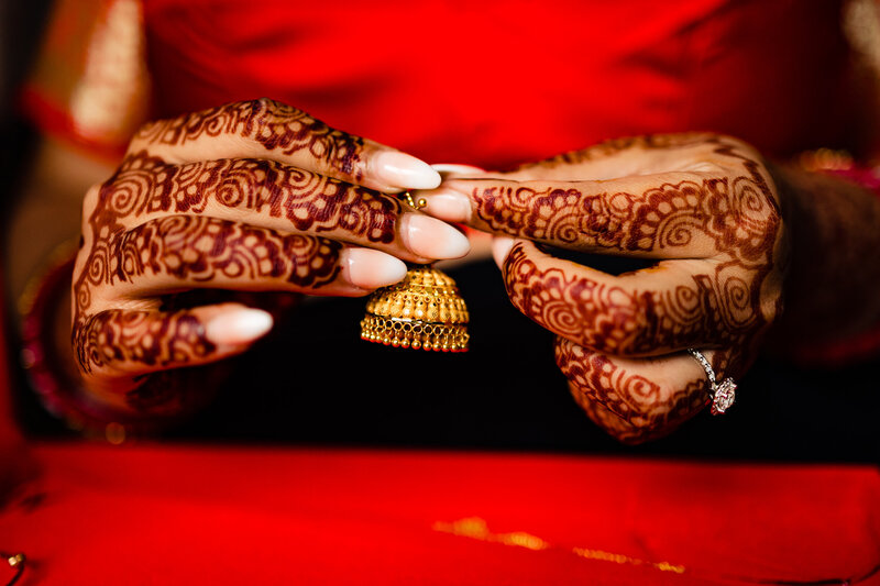 An Indian bride holding a piece of gold jewelry in front of her red dress with her henna covered hands in Detroit Michigan 