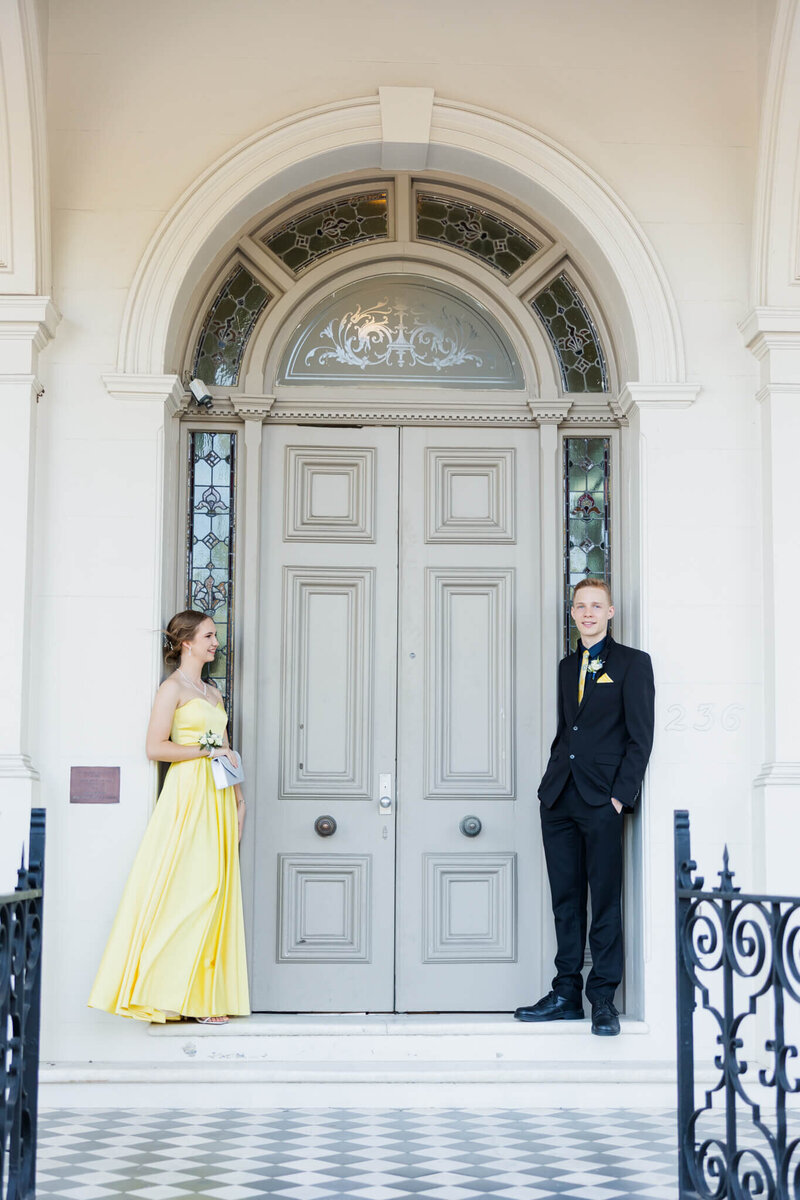 Girl and boy standing at a fancy doorway. Girl in yellow formal dress looking at boy while boy looks towards the camera. Captured by Rockhampton wedding photographer Julie-Anne Photography.