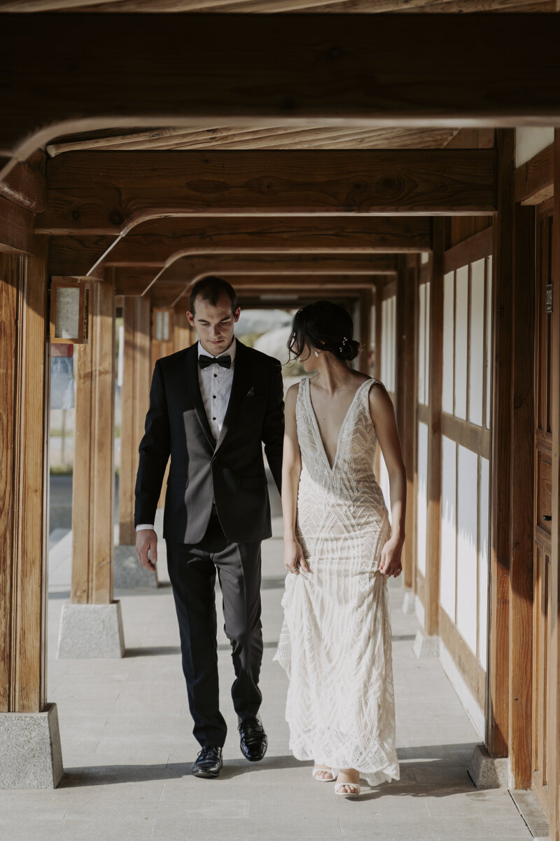 bride dressed in a white wedding dress and groom dressed in a black tuxedo walk to their ceremony