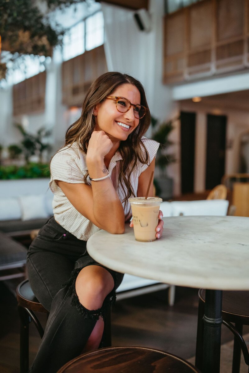woman with iced coffee smiles while sitting at a table