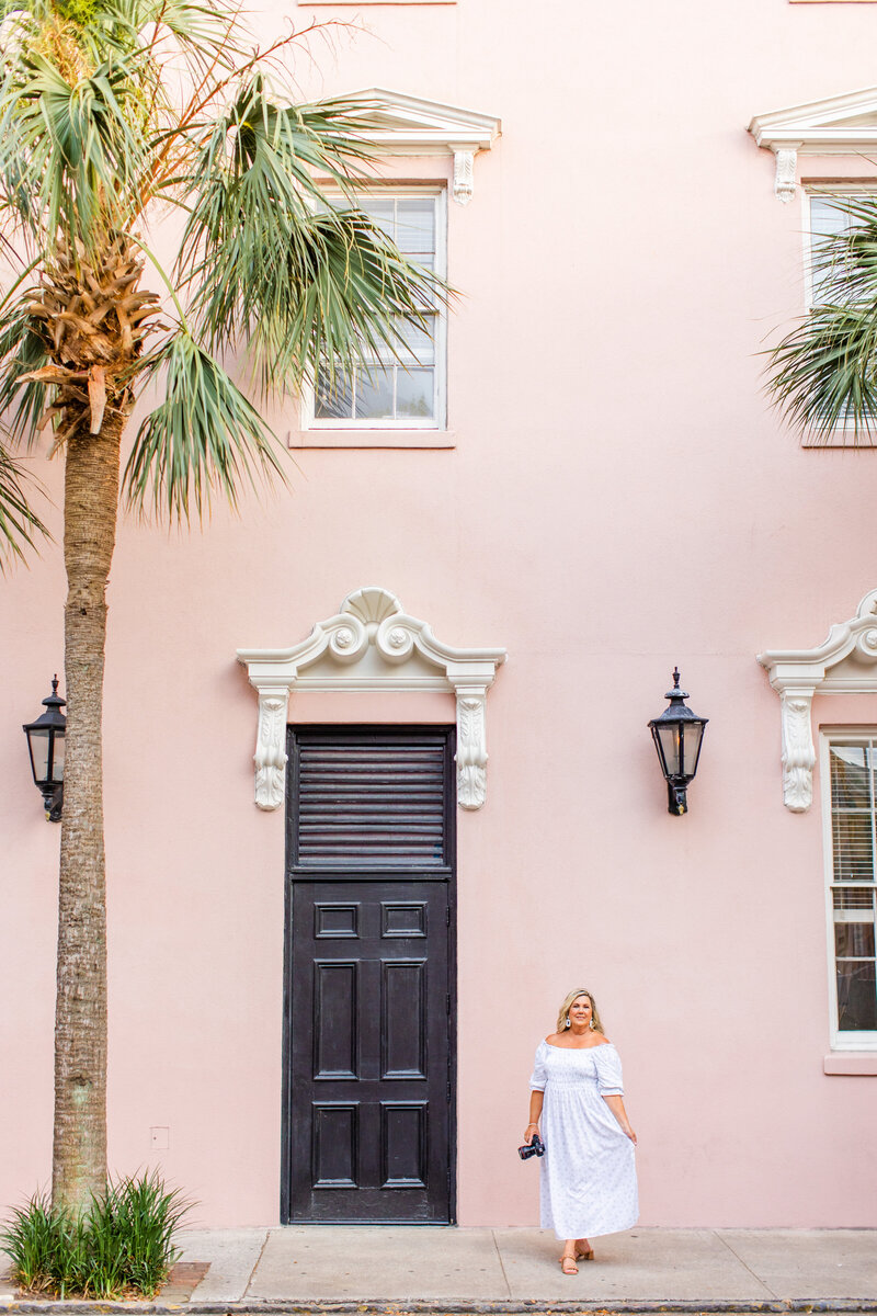 south caorlina photographer posing with blue dress in front of the mills house hotel with a pink background, palm trees and a black door