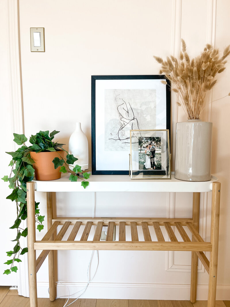 Shelf in Mollie Mason's home decorated with plants, framed photo and art, and a vase