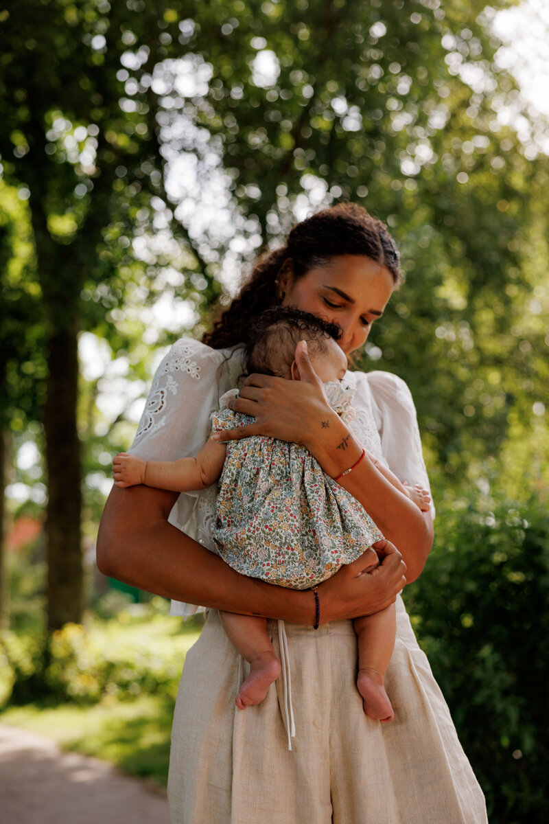 Vrouw houdt een baby liefdevol vast in een groene, rustige omgeving bij Kinderdagverblijf Bij Ons Op De Boerderij.